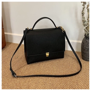 Close-up of black litchi pattern leather and elegant gold metal buckle on a square bag