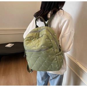 Gros plan d'un sac à dos matelassé vert orné de broderies de nœuds blancs pour un style frais