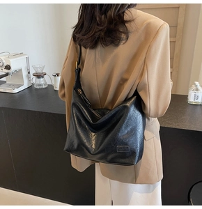 Dettaglio della borsa a mezzaluna in pelle nera indossata con un blazer cammello