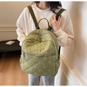 Detail of olive green quilted backpack with white bow embroidery and front zipper pocket