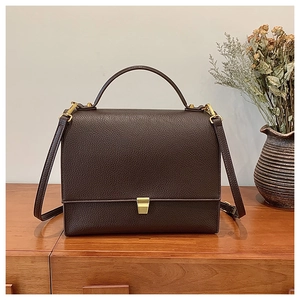 Macro detail of dark brown litchi grain leather texture and gold metal buckle on handbag