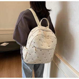 Gros plan du sac à dos matelassé beige avec imprimés nœuds montrant la poche latérale