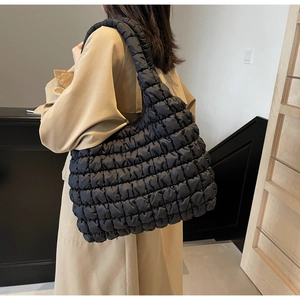 Detailed close-up of black quilted bubble tote bag texture on female model shoulder