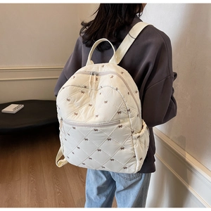 Close-up of cream quilted backpack featuring brown bow embroidery and diamond stitching