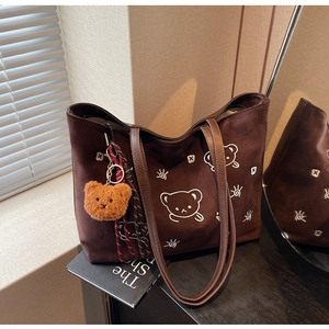 Detail of dark brown suede tote bag with white cartoon bear print and plush charm