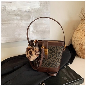 Detail view of a retro bucket bag featuring leopard print, brown leather, and a heart charm
