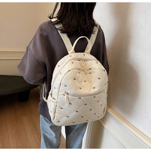Détail d'un sac à dos matelassé beige avec nœuds brodés et texture douce au dos