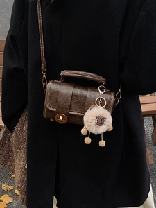 Braune Vintage-Boston-Tasche mit kleinem Plüschschaf-Anhänger auf einem Wollmantel