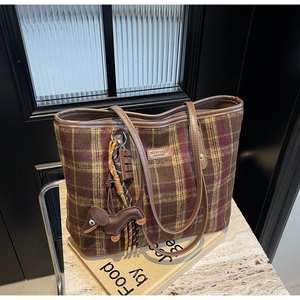Detail of checkered fabric tote bag with leather handle and dachshund charm on stone surface
