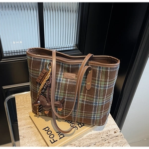 Detail of plaid tote bag with leather handles and decorative chocolate charm on books