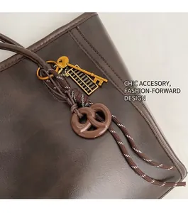 Detail of dark brown leather tote bag featuring a decorative pretzel and key pendant charm