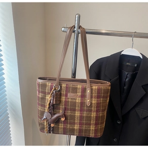 Detail view of plaid tote bag with brown leather straps and dachshund doll charm