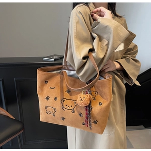 Close-up of brown faux suede tote bag featuring bear embroidery and plush charm