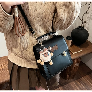 Detail of black leather bag featuring cartoon puppy embroidery and plush bear charm