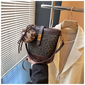 Detail of leopard print bucket bag featuring a golden clasp and plush pompom charm