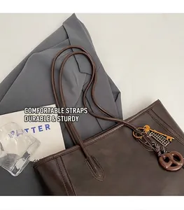 Detail view of large brown faux leather tote bag with elegant golden key pendant charms