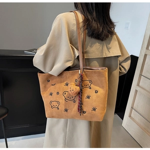 Macro view of brown suede tote bag featuring cartoon bear patterns and plush charm
