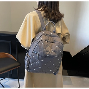 Close-up of grey quilted backpack featuring delicate white bow embroidery and texture