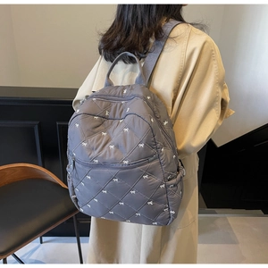 Side view of a grey quilted backpack with white bow embroidery on a model during daily use