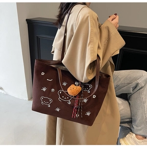 Detail view of brown suede tote bag with cartoon bear print and plush pendant