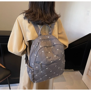 Détail du sac à dos matelassé gris foncé avec broderies de nœuds blancs et poche zippée