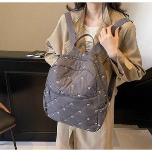 Close-up of gray quilted backpack with embroidered bows and classic diamond stitching detail