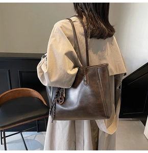 Detail of dark brown leather tote bag with vintage texture and woven tassel pendant