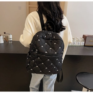 Détail du sac à dos matelassé noir avec imprimés nœuds blancs porté par un modèle
