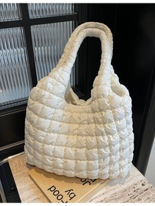 Quilted beige puffer tote bag with square pattern on a marble table background
