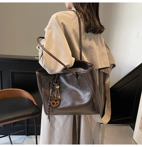 Detail of dark brown leather tote bag featuring stylish charms and a dual-handle design