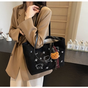 Detail of black suede tote bag featuring cartoon bear print and plush bear accessory