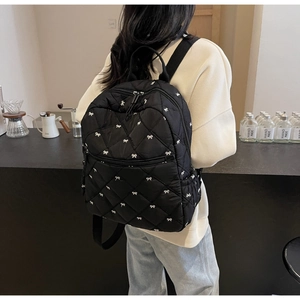 Detail of black quilted backpack featuring white bow pattern in a cozy cafe setting