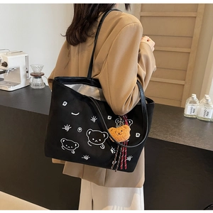 Detail of black suede tote bag featuring a white bear print and plush bear charm