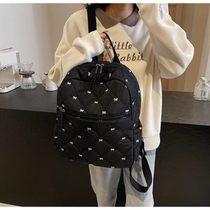 Close-up of black quilted backpack with white bow embroidery and front zipper pocket