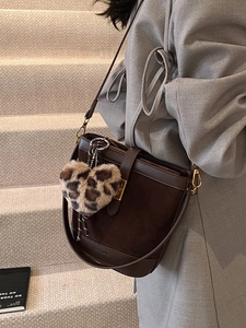 Vintage brown bucket bag with leopard heart charm worn by model on a modern staircase