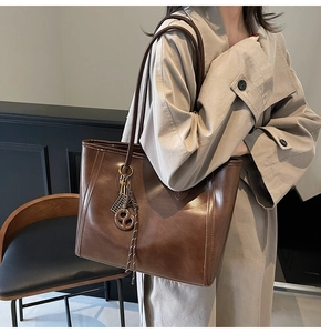 Detailed view of deep brown vintage leather tote bag with braided charm and long strap