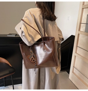 Detail of dark brown vintage leather tote bag with woven charm on beige trench coat