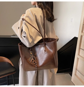Detail shot of vintage brown tote bag featuring knotted braid charm and matte leather texture
