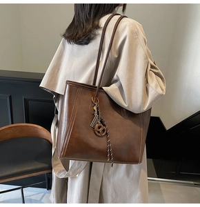 Detail of dark brown leather tote bag with unique charm on model in modern interior