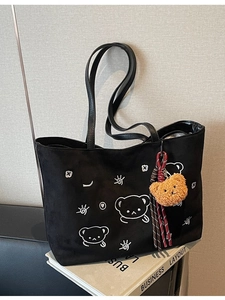 Black suede tote bag with cartoon bear embroidery and plush charm in lifestyle setting