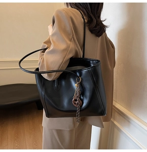 Detail view of large black leather tote bag with brown woven knot charm on shoulder strap