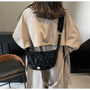 Close-up of black quilted saddle bag with gold metal clasp on a beige trench coat