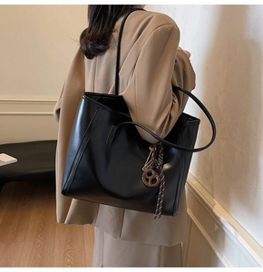 Detail view of large black tote bag with metal key pendant and woven rope accessory