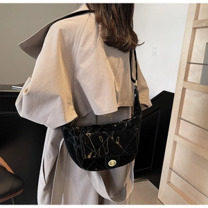 Close-up of a black quilted saddle bag with golden lock on a beige trench coat
