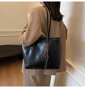 Close-up of black leather tote bag with brown ring charm on khaki blazer outfit