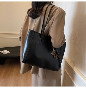 Detail of minimalist black leather tote bag with elegant straps and circular charm detail