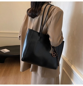 Detail of black matte leather tote bag featuring a decorative charm and long straps