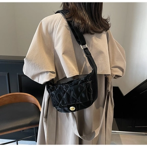 Detail of a black quilted saddle bag with gold clasp shown on a beige trench coat