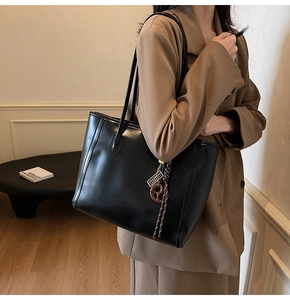Detail of black leather tote bag with side metal charm and contrast tassel decoration
