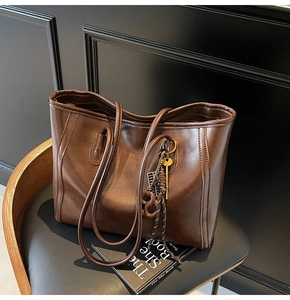 Detail of deep brown faux leather tote bag with gold key tag on a leather chair
